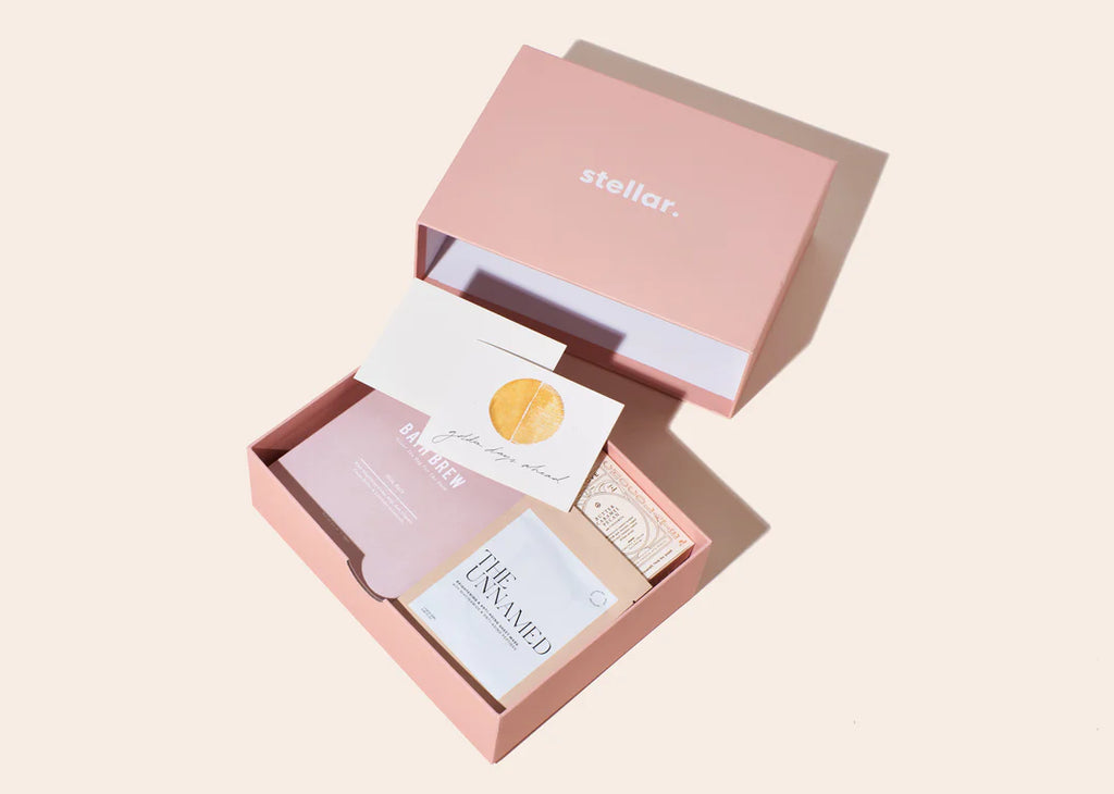 top down photo of a Soak Trio gift set: pink cardboard box with a sheet mask, soap, and other self care items inside.
